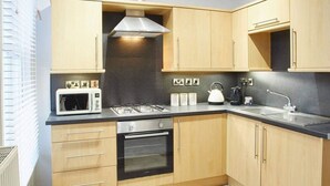 A compact kitchen with wooden cabinets, a built-in oven, a microwave, a gas stove, and a stainless steel range hood.