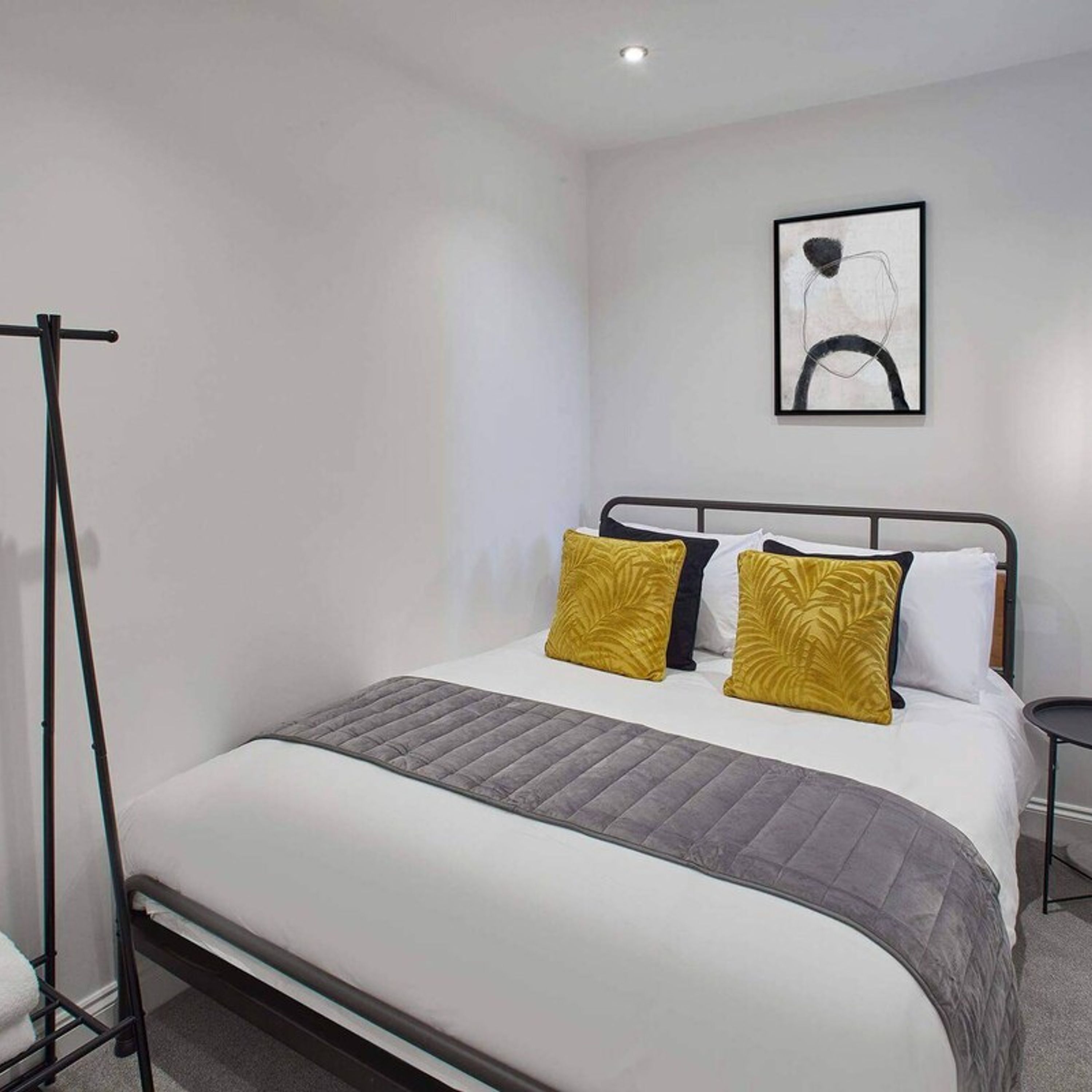 A modern hotel room with a single bed, a standing lamp, and a framed abstract artwork on the wall.