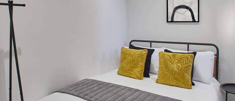 A modern hotel room with a single bed, a standing lamp, and a framed abstract artwork on the wall.
