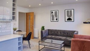 A modern living room with a grey sofa, a glass coffee table, and a red armchair. There are two abstract wall art pieces and a wooden door leading to another room. - Host Stay Apartment Two Hudsons Yard House (Whitby)