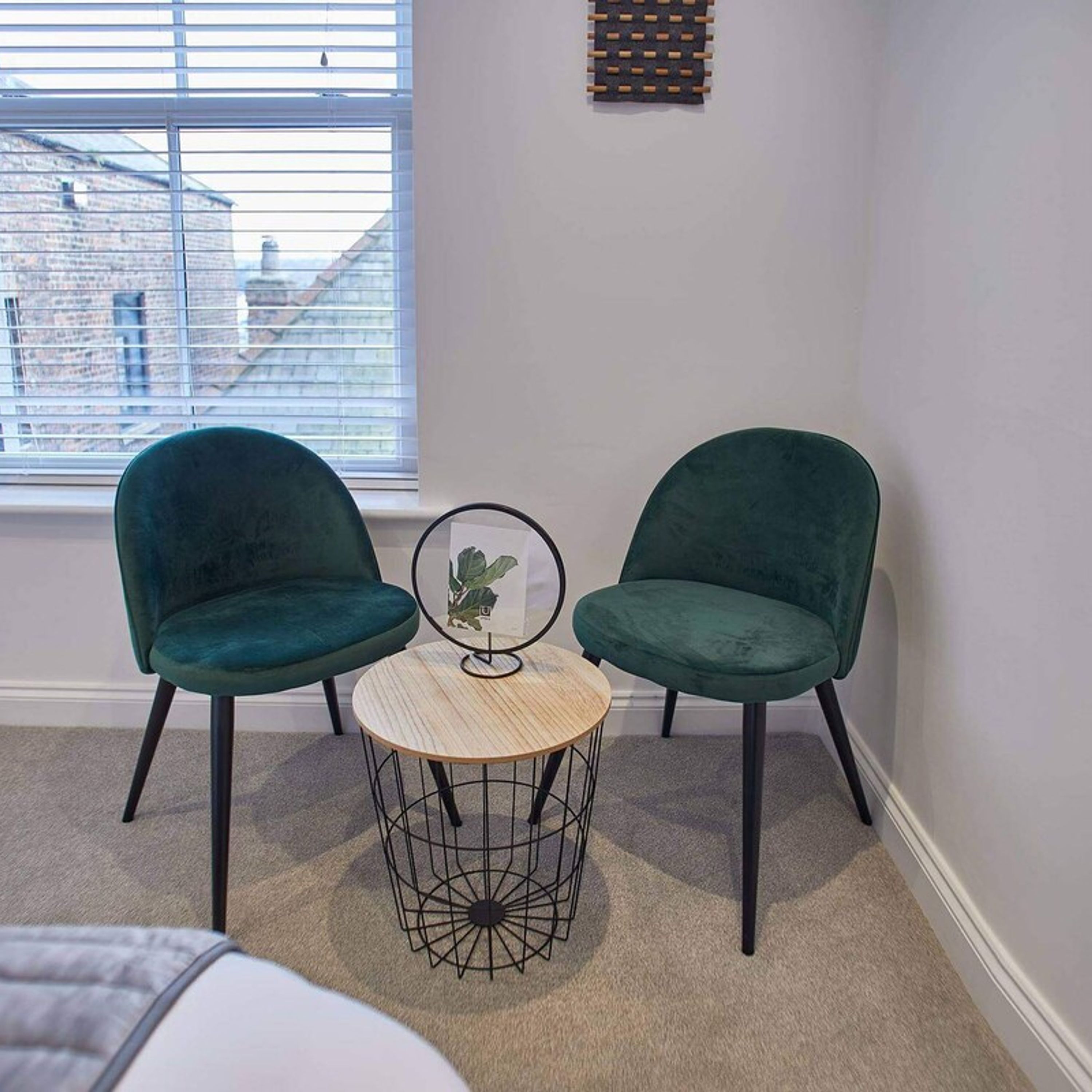 A corner room with two green chairs, a small round table, and a window with blinds.
