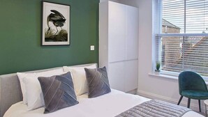 A bedroom with a bed, pillows, a framed picture on the wall, a window with blinds, and a chair. - Host Stay Apartment Two Hudsons Yard House (Whitby)
