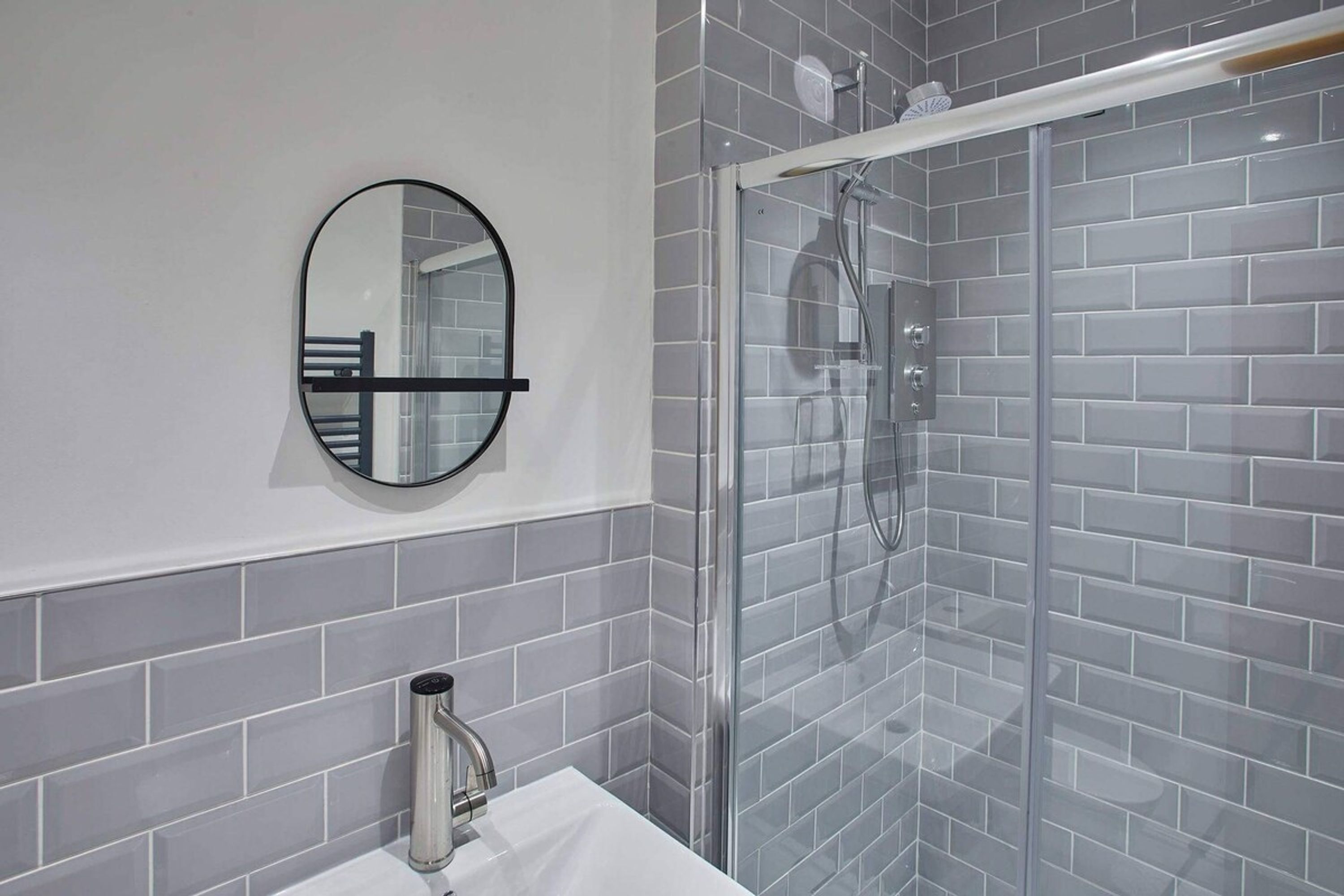 Een badkamer met een wit wastafel, een ronde spiegel en een douche met glazen wanden.