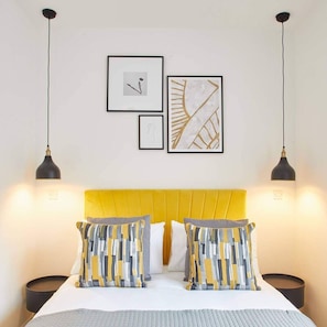 Une chambre d’hôtel avec un lit, deux tables de chevet et trois œuvres d’art encadrées accrochées au mur.