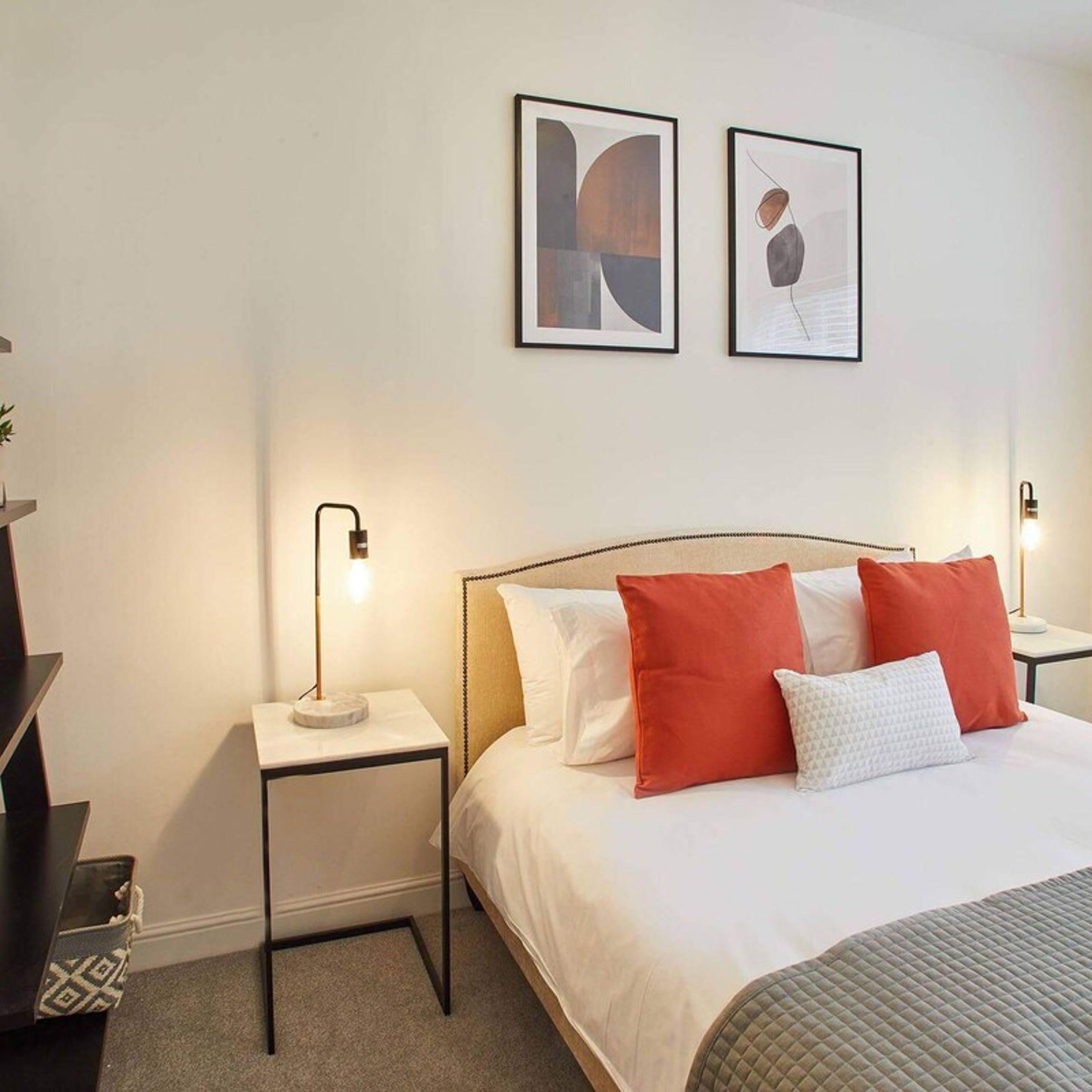 Ein Hotelzimmer mit einem Bett, zwei Nachttischen, zwei gerahmten Kunstwerken an der Wand.