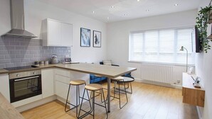 Eine moderne Küche mit einer zentralen Kochinsel, Barhocker, einem eingebauten Backofen und einem Fenster mit Jalousien.