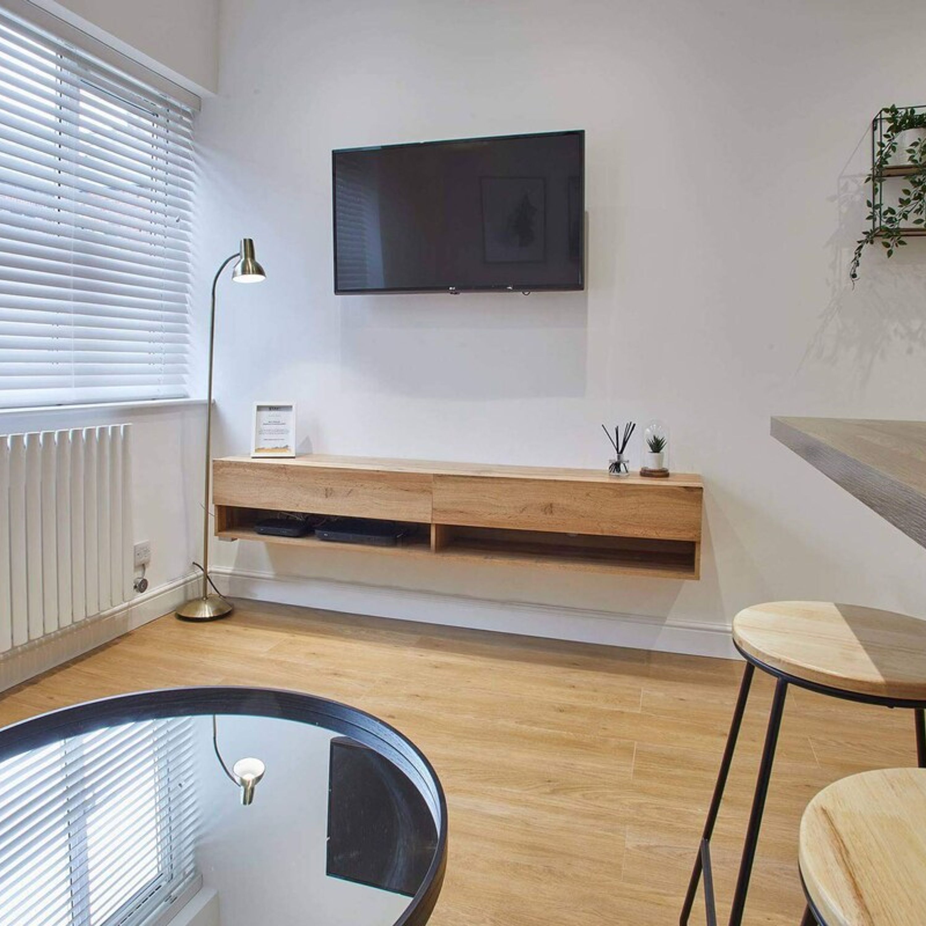 A modern living room with a flat-screen TV mounted on the wall, a wooden console table below, a glass coffee table, and a bar stool.
