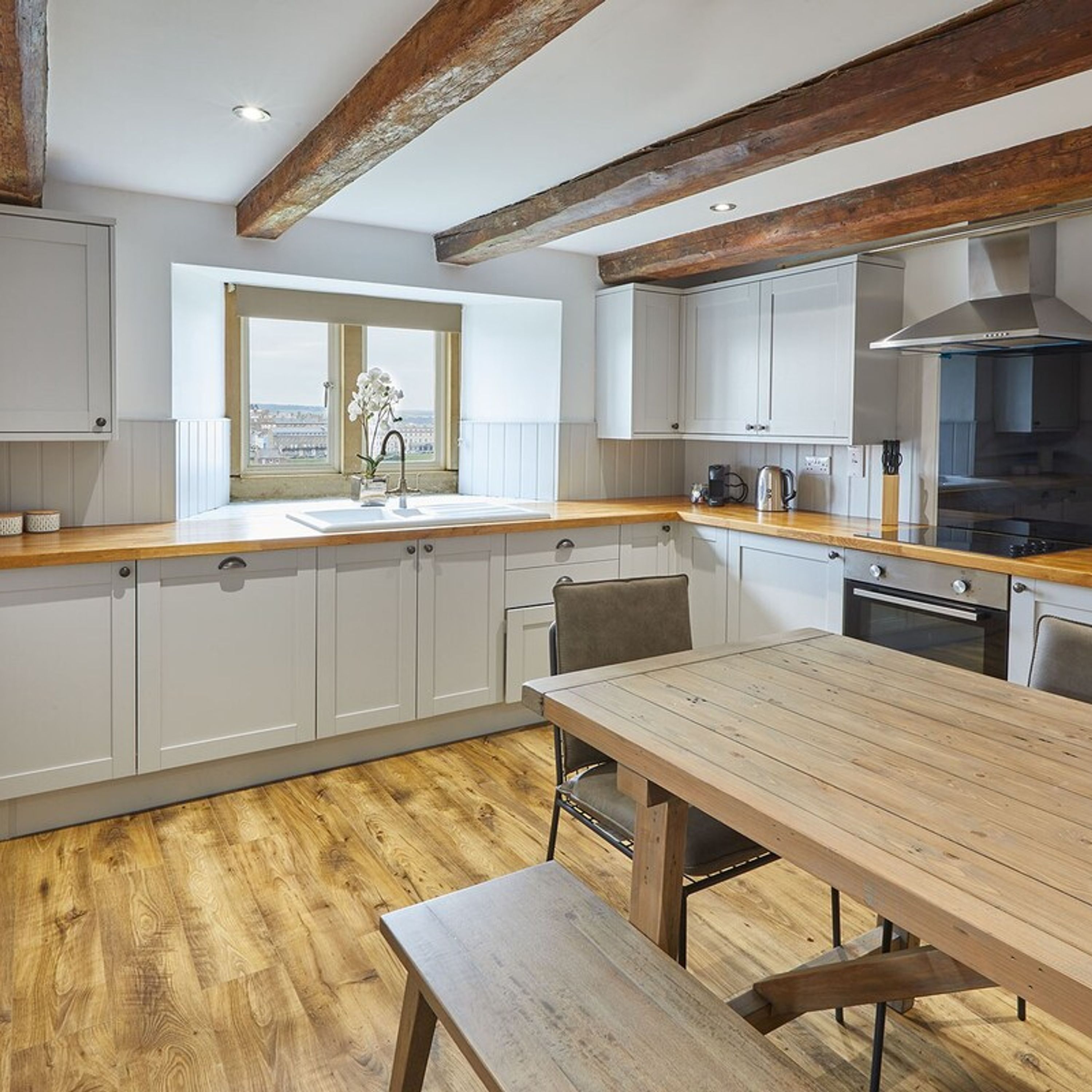 A modern kitchen with white cabinets, a wooden countertop, and a large window offering a view.