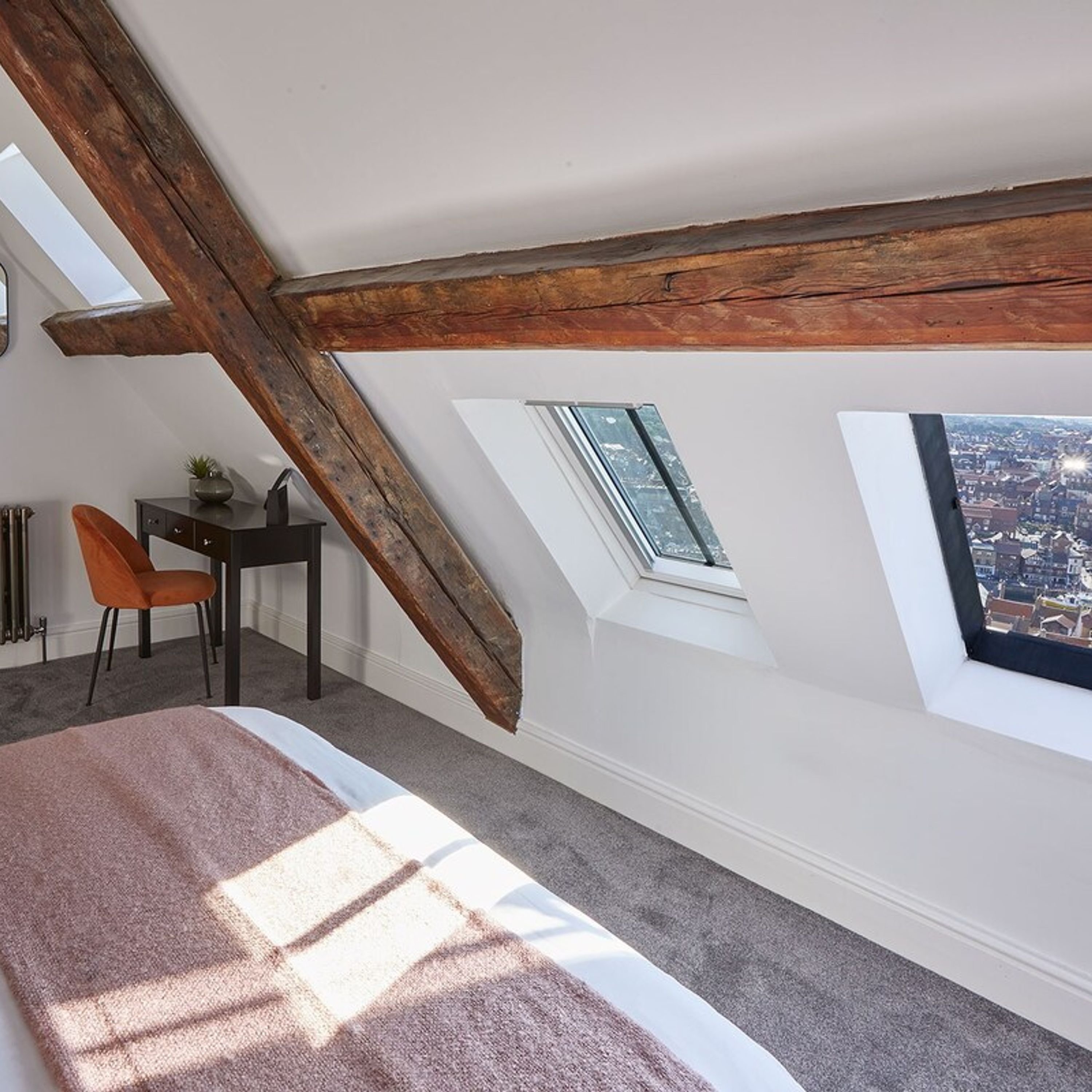 A bedroom with a sloped ceiling, a skylight, a bed, a desk, and a chair.
