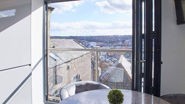 A modern room with a large window, a round table with a potted plant, and a view of a cityscape. - Host Stay The View Hudsons Yard House (Whitby)