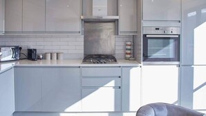 A modern kitchen with white cabinetry, a gas stove, an oven, and a coffee maker. - Host Stay The View Hudsons Yard House (Whitby)