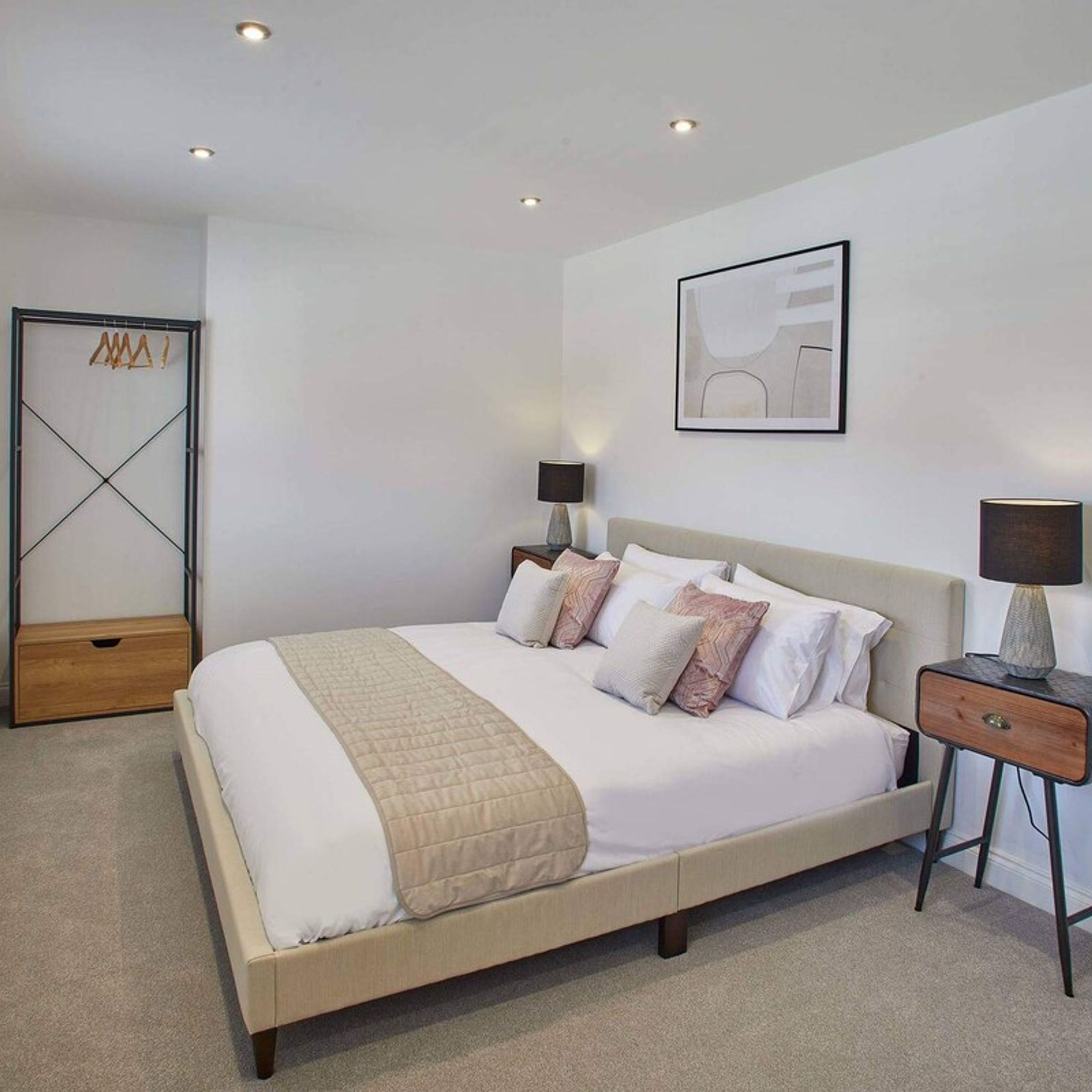 A modern bedroom with a large bed, bedside lamps, a framed artwork, and a wooden storage unit.