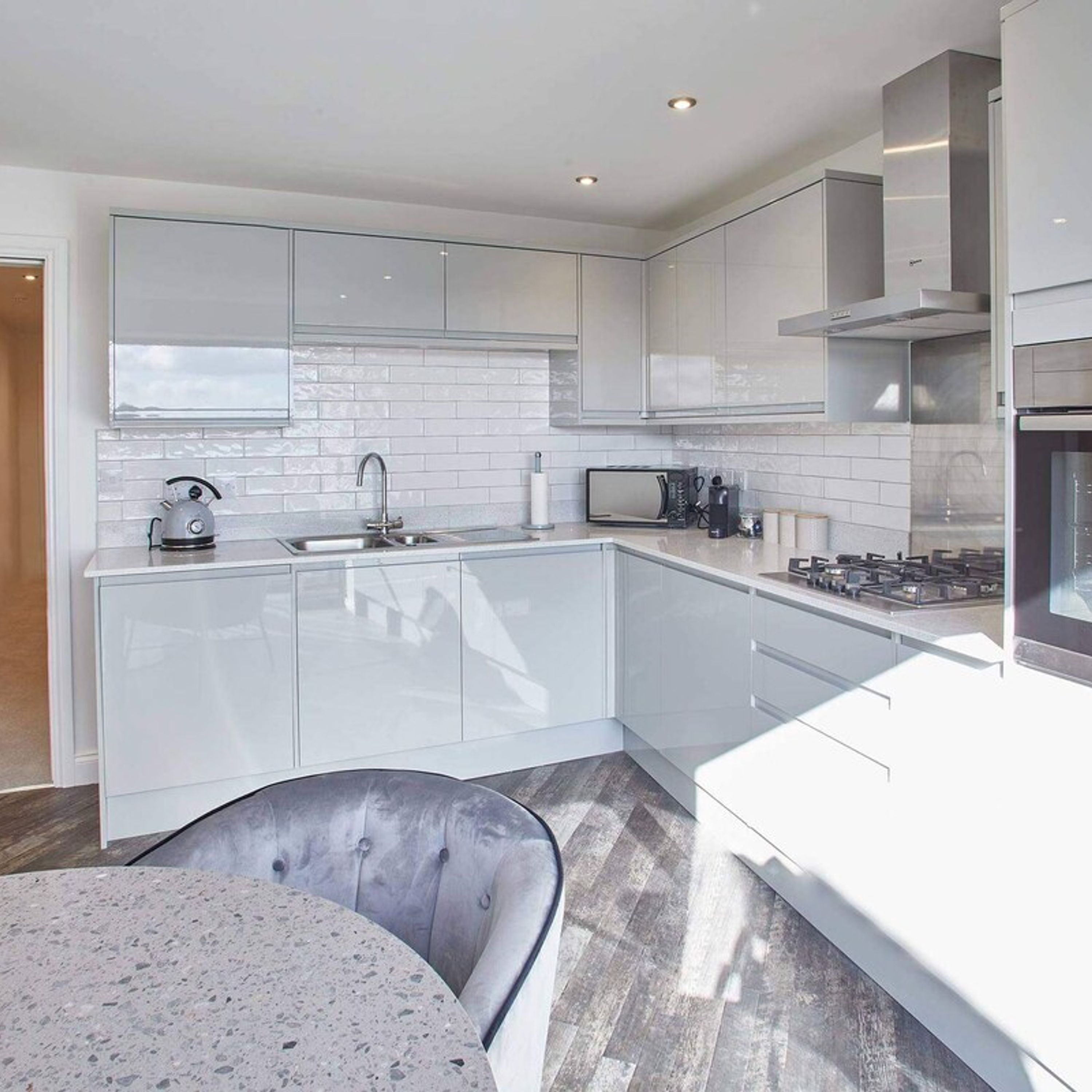 A modern kitchen with white cabinetry, a stainless steel range hood, and a built-in microwave.