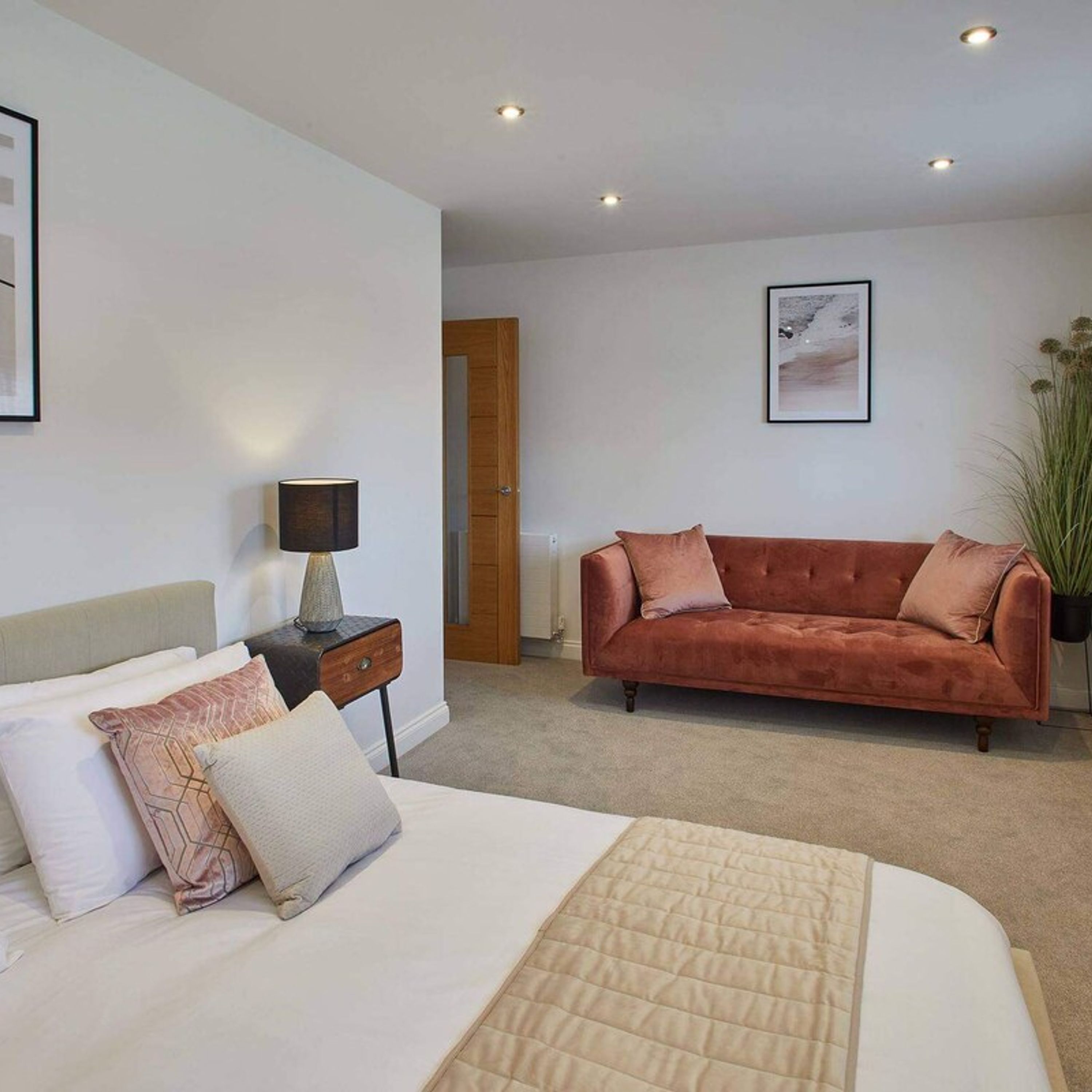 A bedroom with a bed, a nightstand, a lamp, a sofa, and a door.