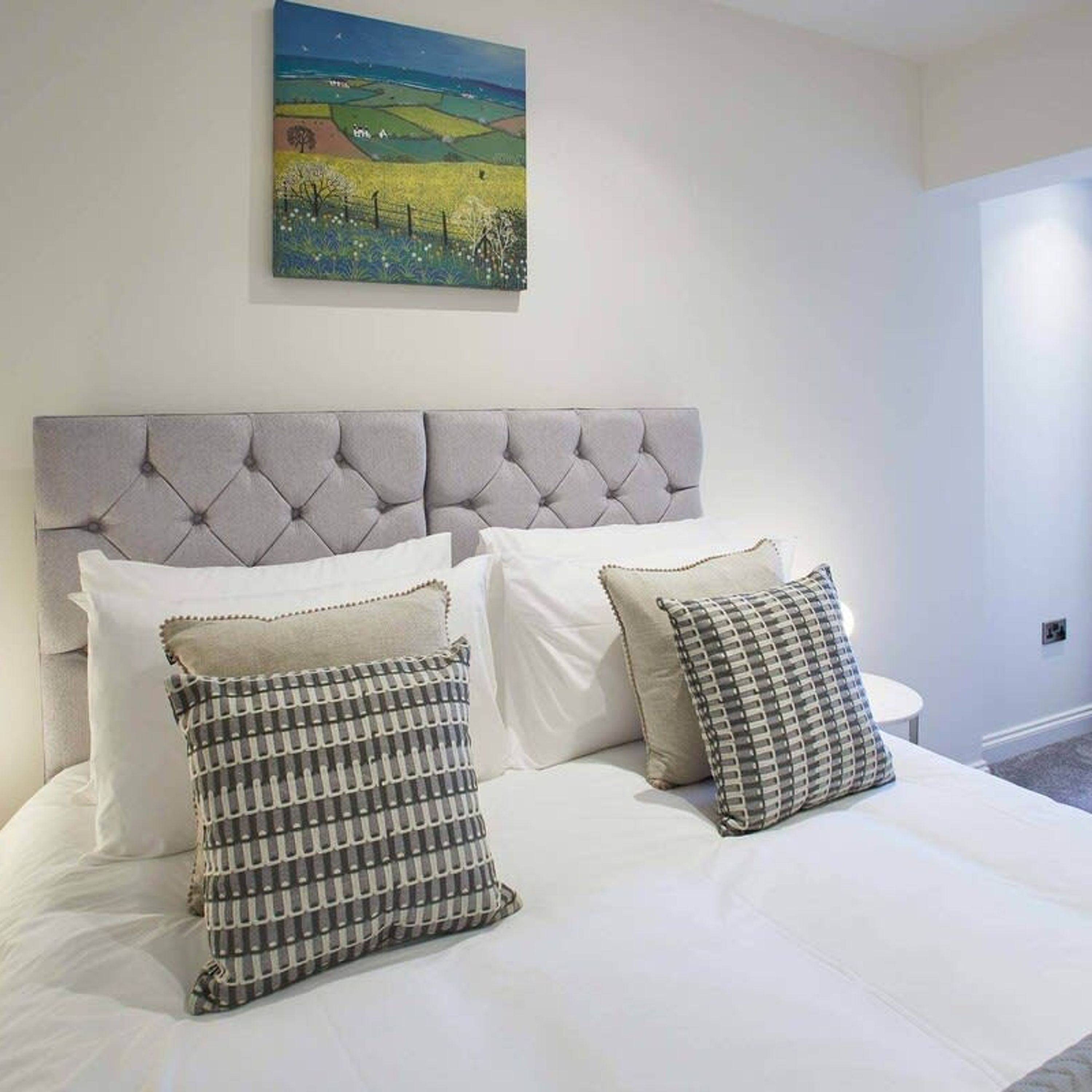 A bedroom with a tufted headboard, white bedding, and two patterned pillows.