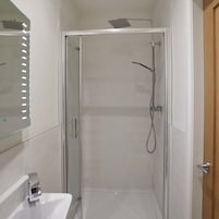 Un baño moderno con cabina de ducha de vidrio, un lavamanos blanco y un espejo con luces.