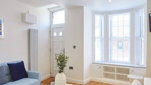 A modern living room with a light blue sofa, a white coffee table, and a white armchair. There is a radiator, a door, and a window with blinds. - Host Stay The Old Sweet Shop (Whitby)