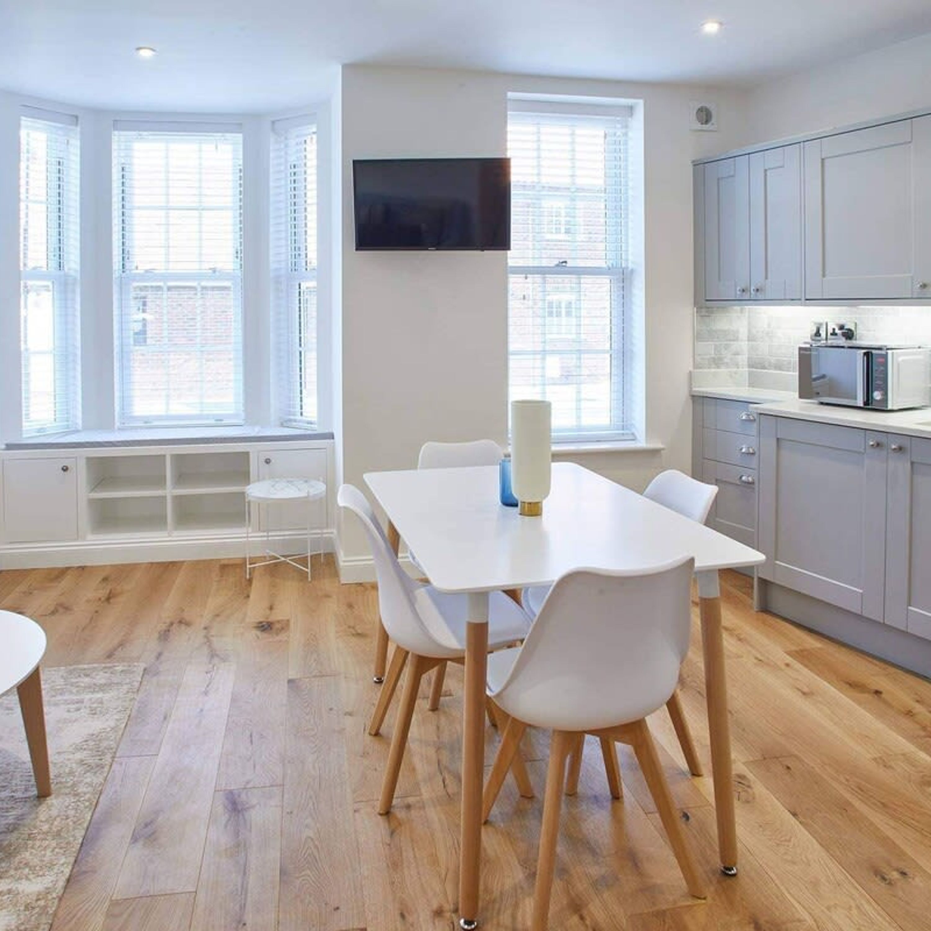 Une cuisine moderne avec des armoires blanches, un four à micro-ondes encastré et un coin repas comprenant une table et des chaises blanches.