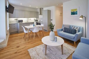 Una sala de estar moderna con un sofá azul claro, una mesa de centro blanca y un comedor con mesa y sillas blancas.