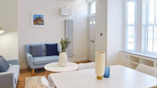 A modern living room with a white table, white chairs, a blue sofa, and a radiator. - Host Stay The Old Sweet Shop (Whitby)