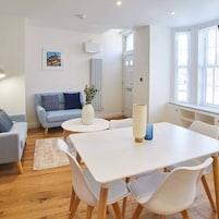 Un salón moderno con una mesa blanca, sillas blancas, un sofá azul y un radiador.