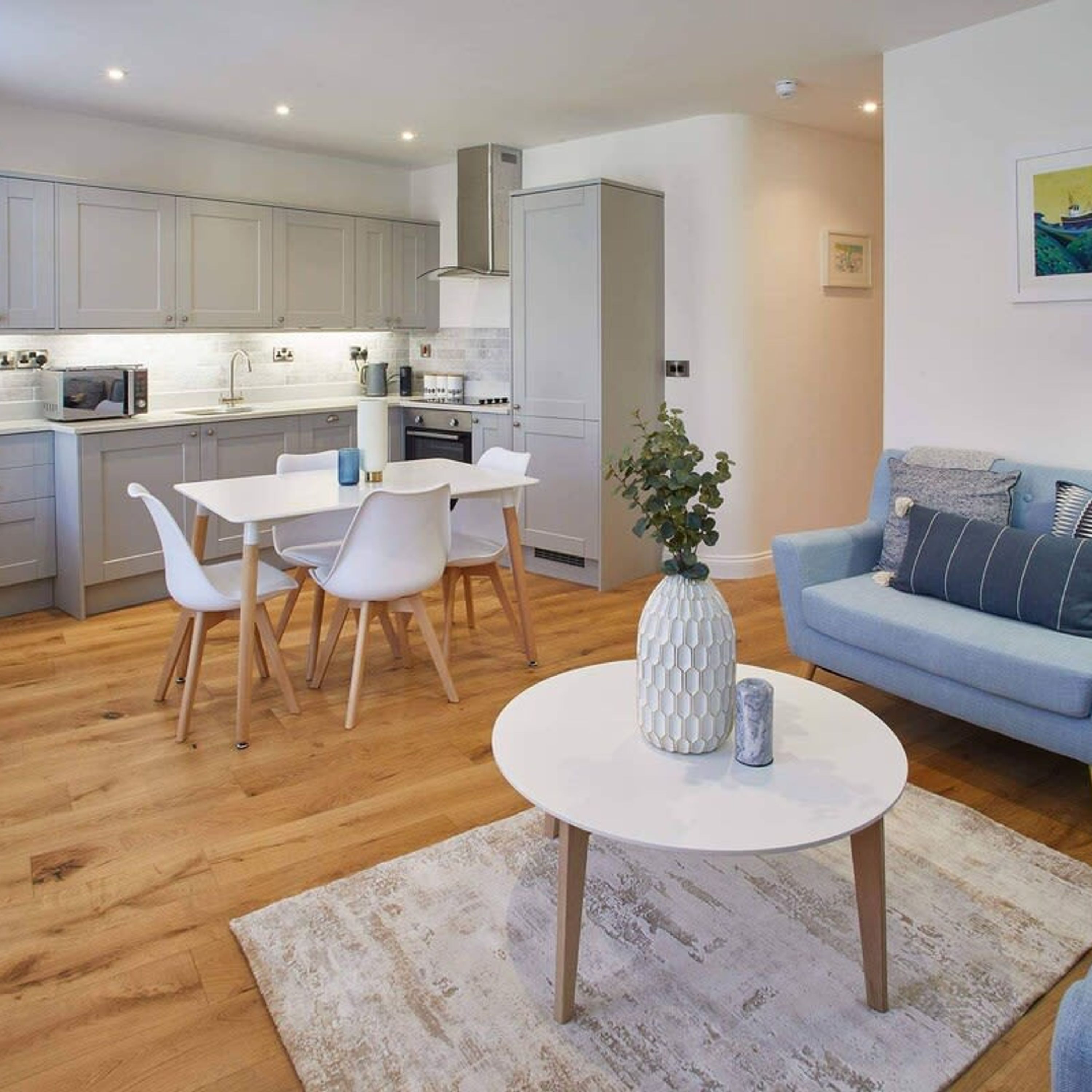 A modern living room with a blue sofa, a white coffee table, and a dining area with white chairs and a white table.