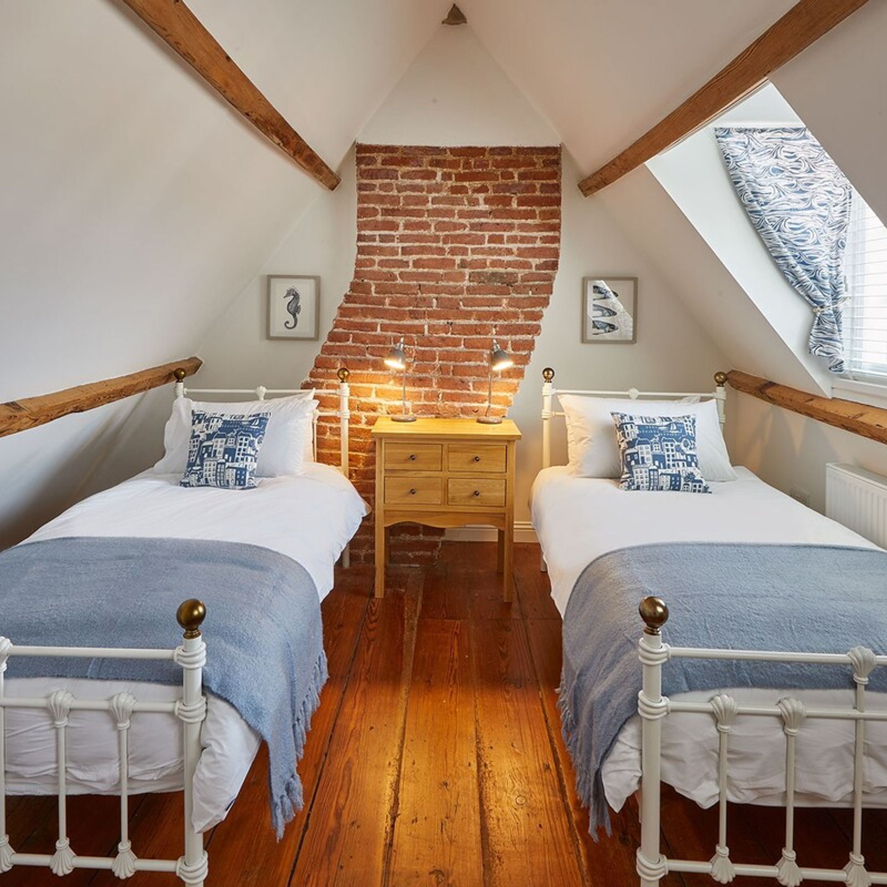 A bedroom with two beds, a wooden floor, a brick wall, and a skylight.