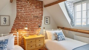 Une chambre avec deux lits, un mur en briques, des poutres en bois, une fenêtre avec des stores et une table de chevet avec des lampes.