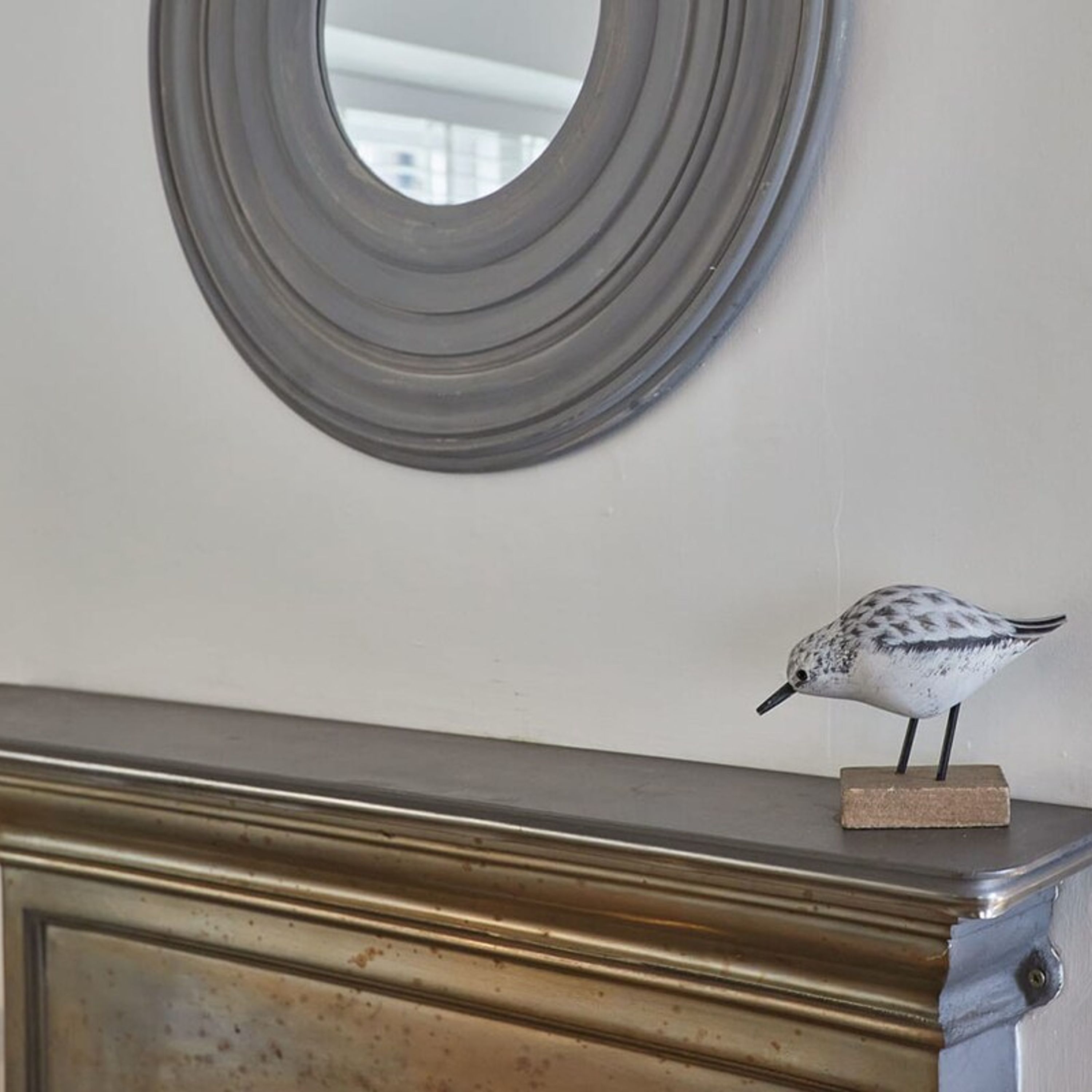 A decorative bird on a dresser with a mirror above it.
