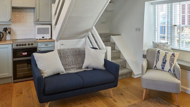 Un salon moderne avec un canapé bleu, un fauteuil gris, un escalier et un coin cuisine équipé d’un four à micro-ondes.