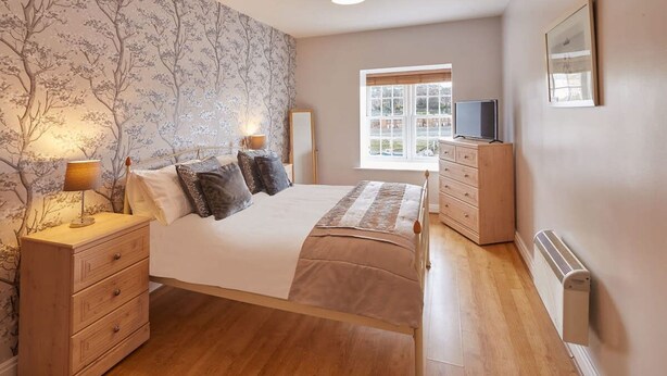 A bedroom with a bed, bedside tables, a dresser, a radiator, a window with a view, and a TV.