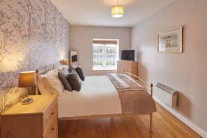 Classic bedroom with a large bed, nightstand, dresser, and television.