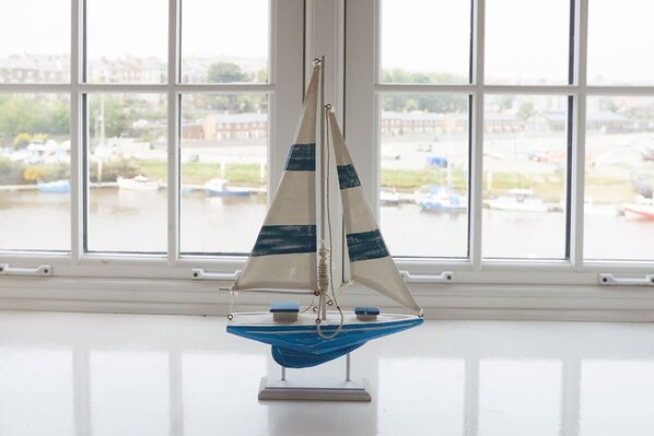 A model sailboat on a stand in front of a window with a view of a river and boats. - Host Stay Seal Watch (Whitby)