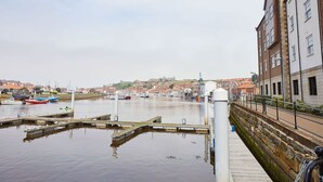 A waterfront marina with boats docked, a stone wall, and buildings in the background.