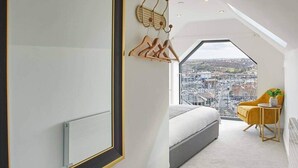 A bedroom with a large mirror, a bed, a chair, and a view of the city through a skylight.