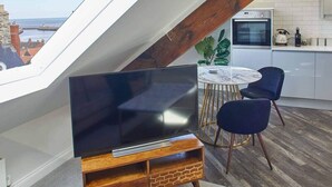 A modern loft bedroom with a skylight, a TV, a dining area, and a kitchen.
