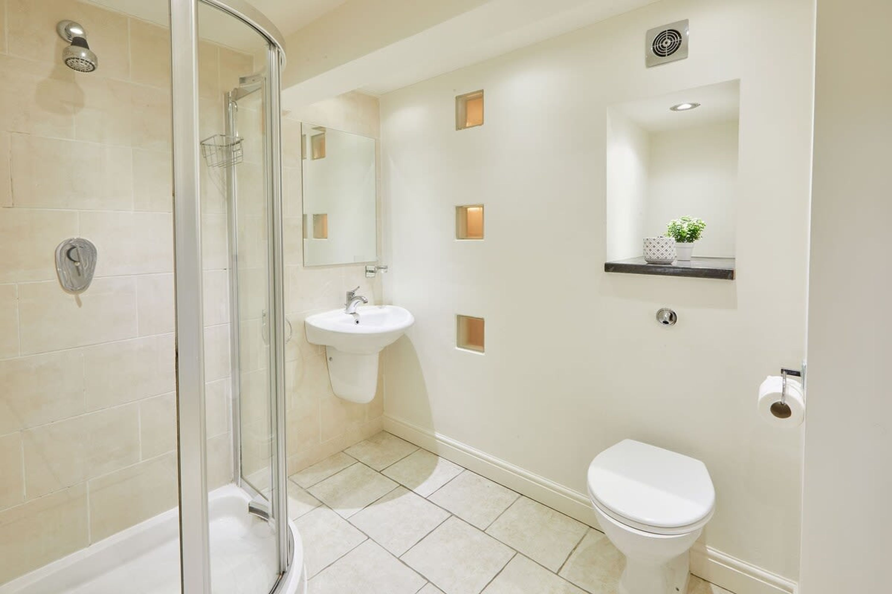 A modern bathroom with a glass shower enclosure, a white sink, a toilet, and a mirror.