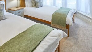 A hotel room with two beds, a bedside table with a lamp, a framed picture on the wall, and a large window with sheer curtains.