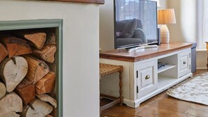A living room with a fireplace, a television on a wooden stand, and a window with curtains.