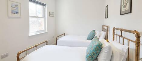 A bedroom with two single beds, a window, and framed pictures on the walls.