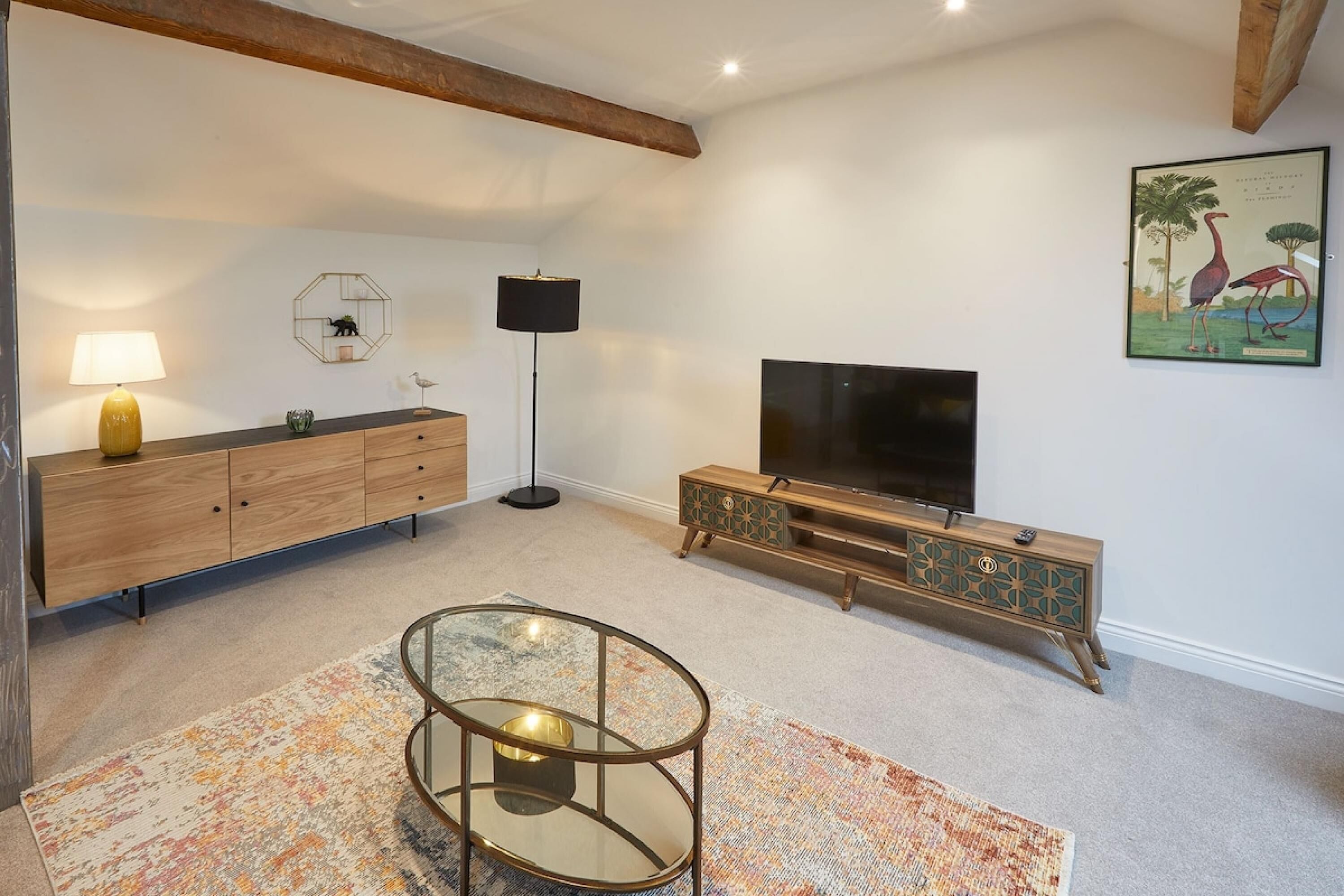 Una sala de estar con un aparador de madera, una mesa de centro de vidrio, un televisor y una alfombra estampada.