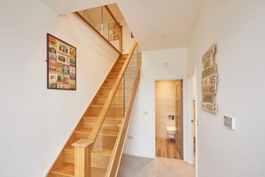 A modern staircase with wooden steps and glass railings, leading to a door.