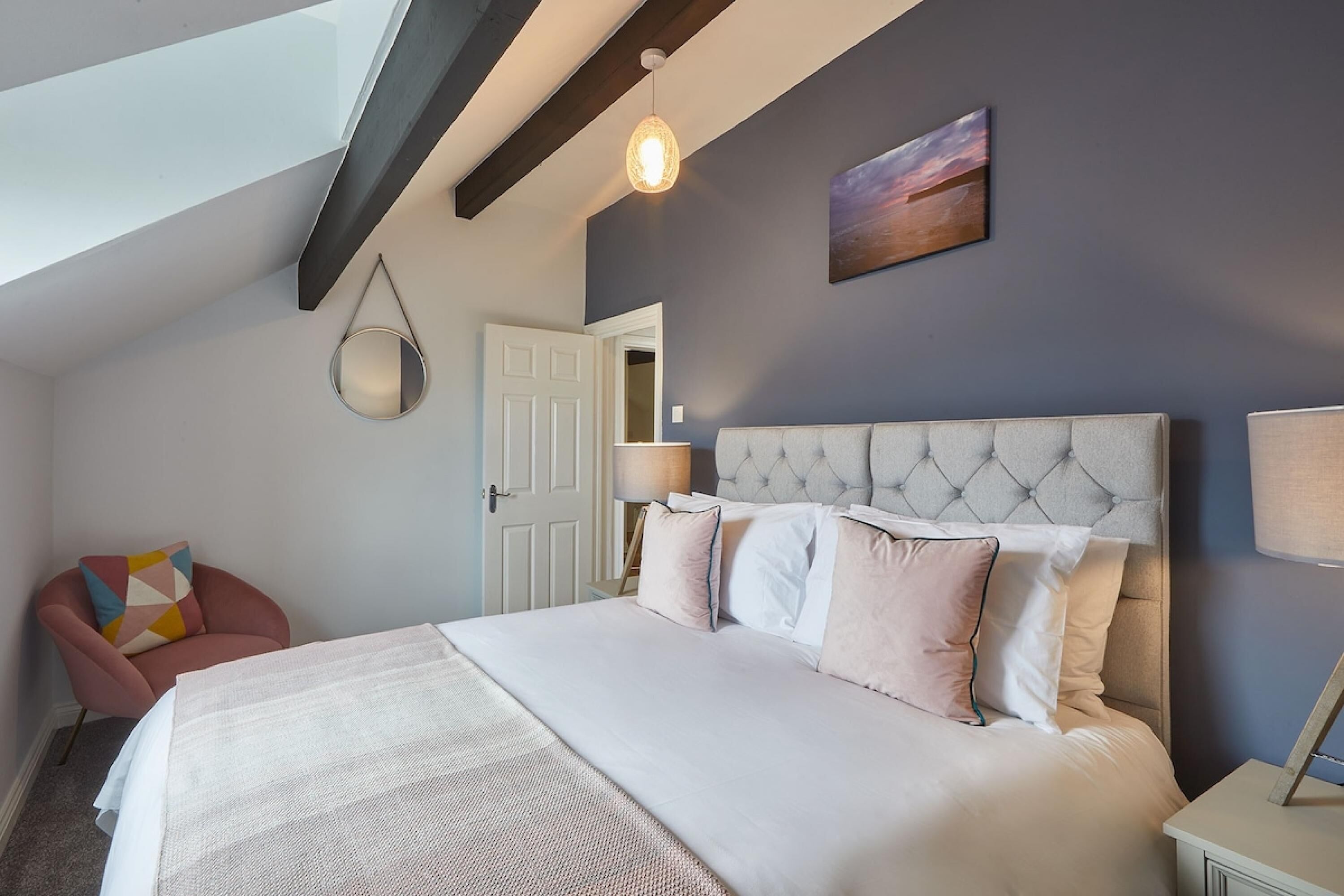 A bedroom with a large bed, a chair, a hanging light fixture, and a door.