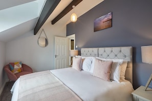 A bedroom with a large bed, a chair, a hanging light fixture, and a door.