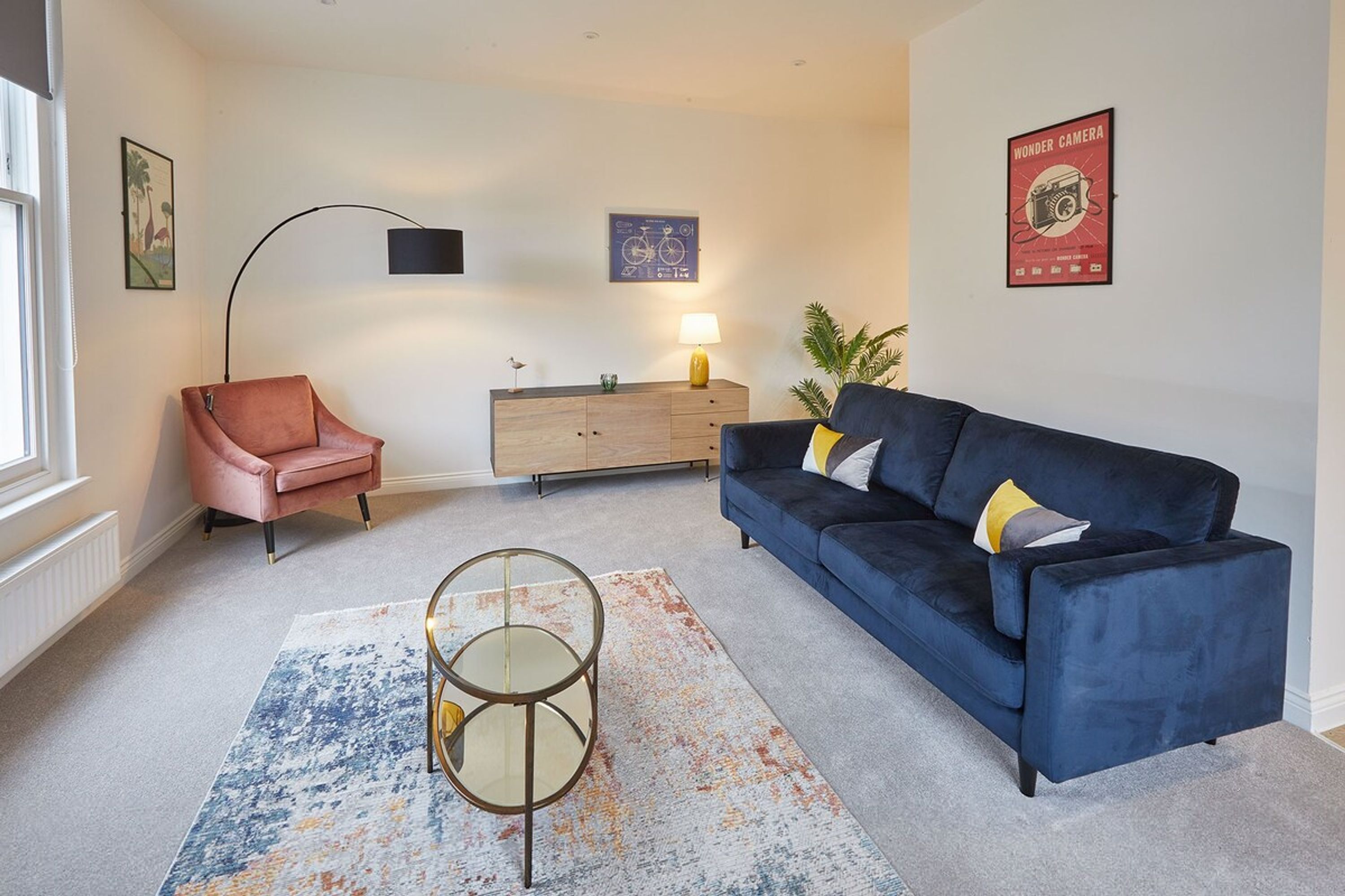 A modern living room with a blue sofa, a pink chair, a wooden cabinet, and a round coffee table.