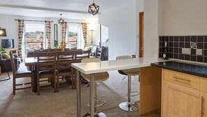 Et moderne køkken med spiseplads, der har en stor ø, træskabe og udsigt gennem den åbne dør.