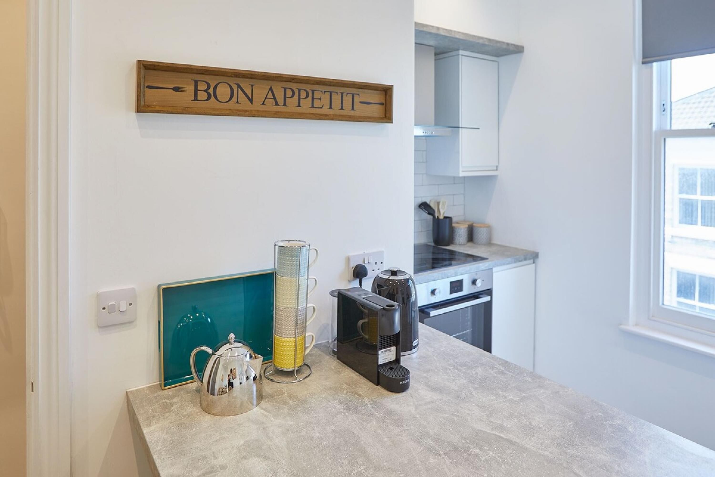 A kitchen with a coffee maker, a kettle, and a coffee grinder on the counter. There is a sign above the counter that reads "BON APPETIT".