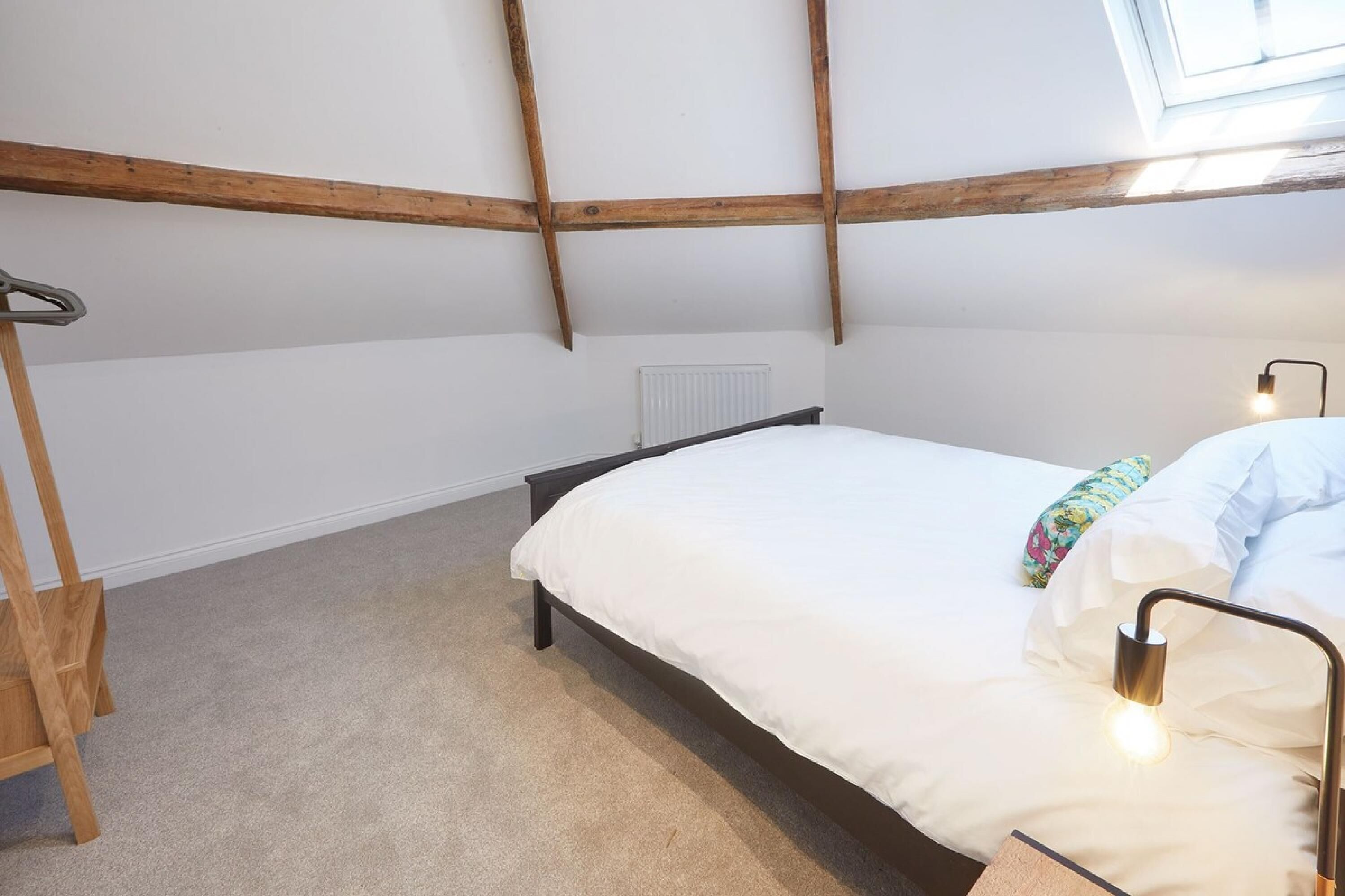 Un dormitorio con cama, radiador, escalera de madera y tragaluz.