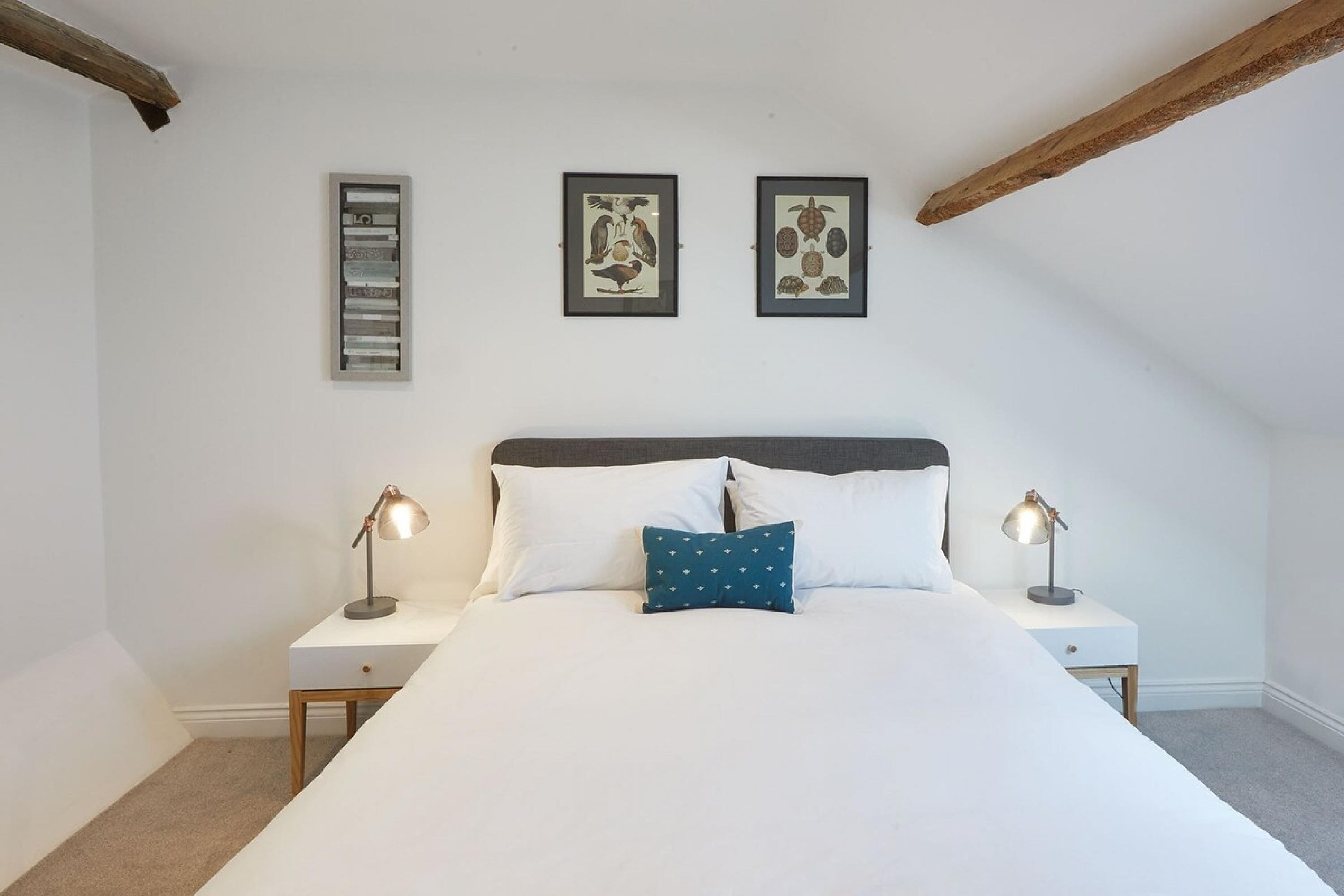 A bedroom with a large bed, two bedside tables, and three framed pictures on the wall.