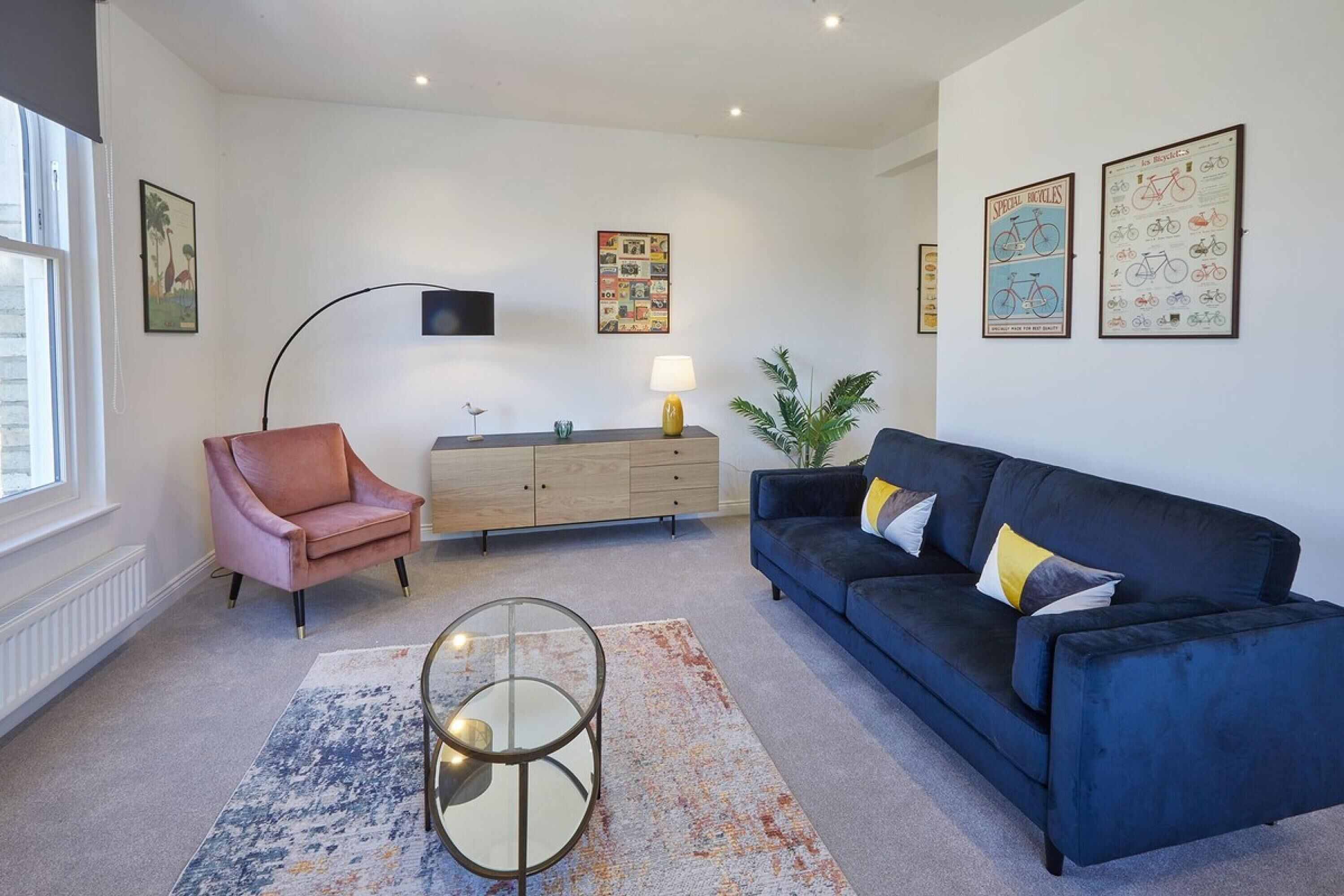 A modern living room with a blue sofa, a pink armchair, a glass coffee table, and a wooden cabinet.
